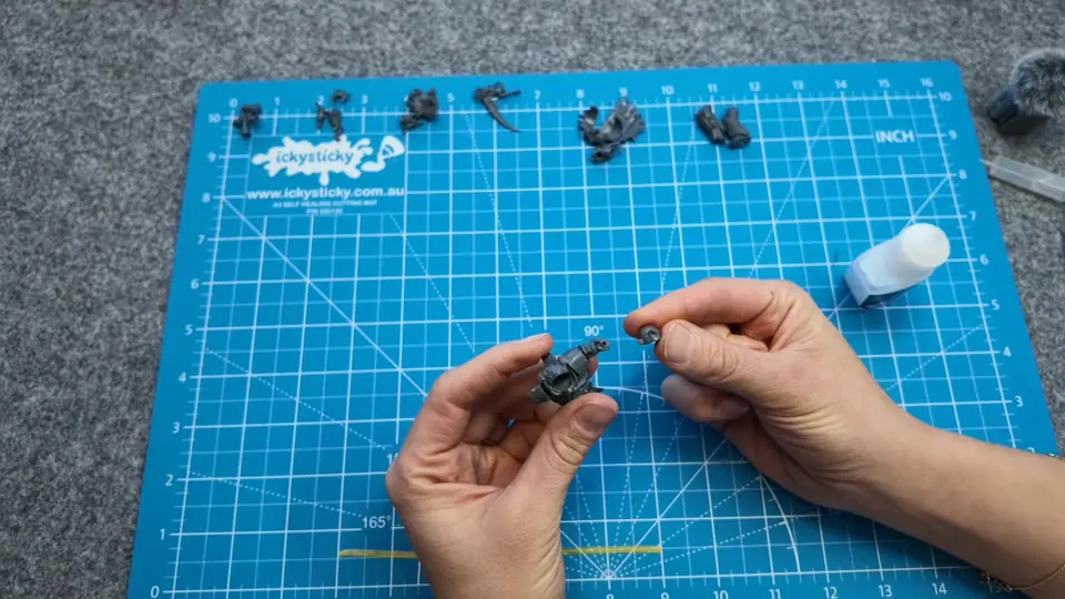 Gluing the parts of her Death Guard miniature together on a cutting mat, glue bottle beside her, Episode 03