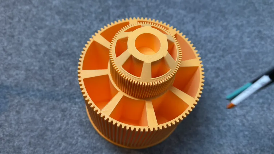 An orange 3D-printed paint carousel on her desk with a brush beside it, Episode 01