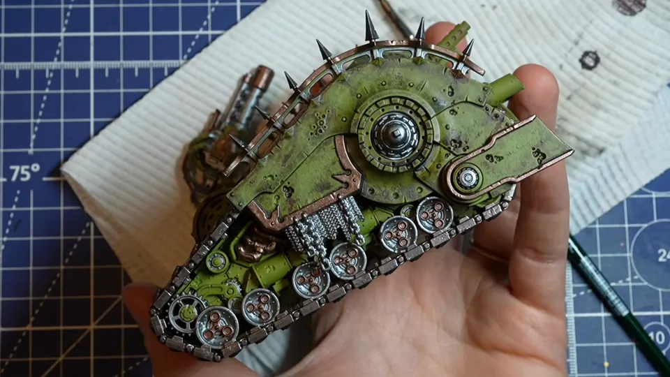 The tank side with silver tracks, chains and wheels and copper trims freshly base coated, held in her hand, Episode 07